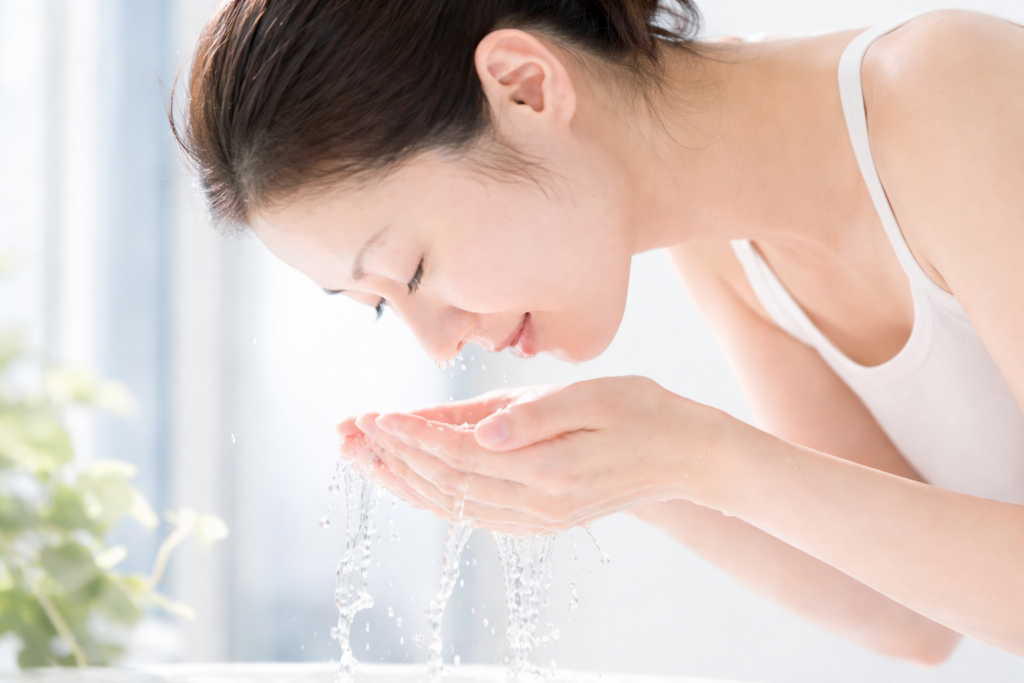 깊은 보습과 수분 충전 표현: 물이 얼굴 위로 쏟아지며 환하게 웃는 여성, 요좁크림 스킨케어 루틴을 상징하는 청량하고 촉촉한 피부 이미지