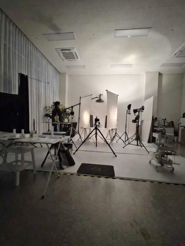 넓은 스튜디오 현장에서 농낭크림 제품 촬영이 한창인 모습입니다. 중앙에 설치된 메인 카메라와 여러 대의 전문 조명, 반사판이 제품 하나를 위해 정교하게 배치되어 있으며, 현장의 열기와 전문성이 고스란히 느껴지는 비하인드 컷입니다.